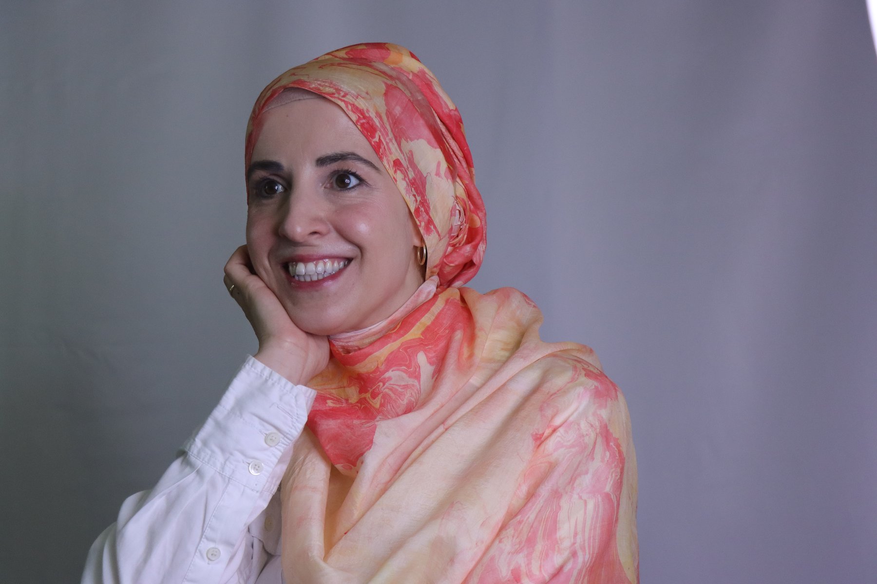 Zeynep Guvenc smiling in a hand-marbled silk scarf in coral, peach, and gold tones