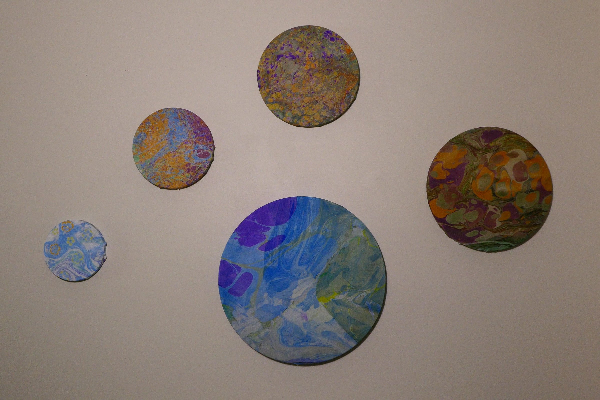 Wall installation of five marbled round panels by Zeynep Guvenc, varying in size and pattern
