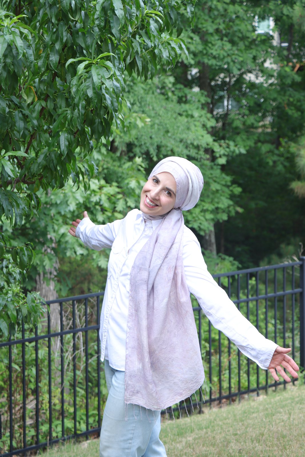Zeynep Guvenc smiling with open arms in a garden, wearing one of her hand-marbled silk scarves