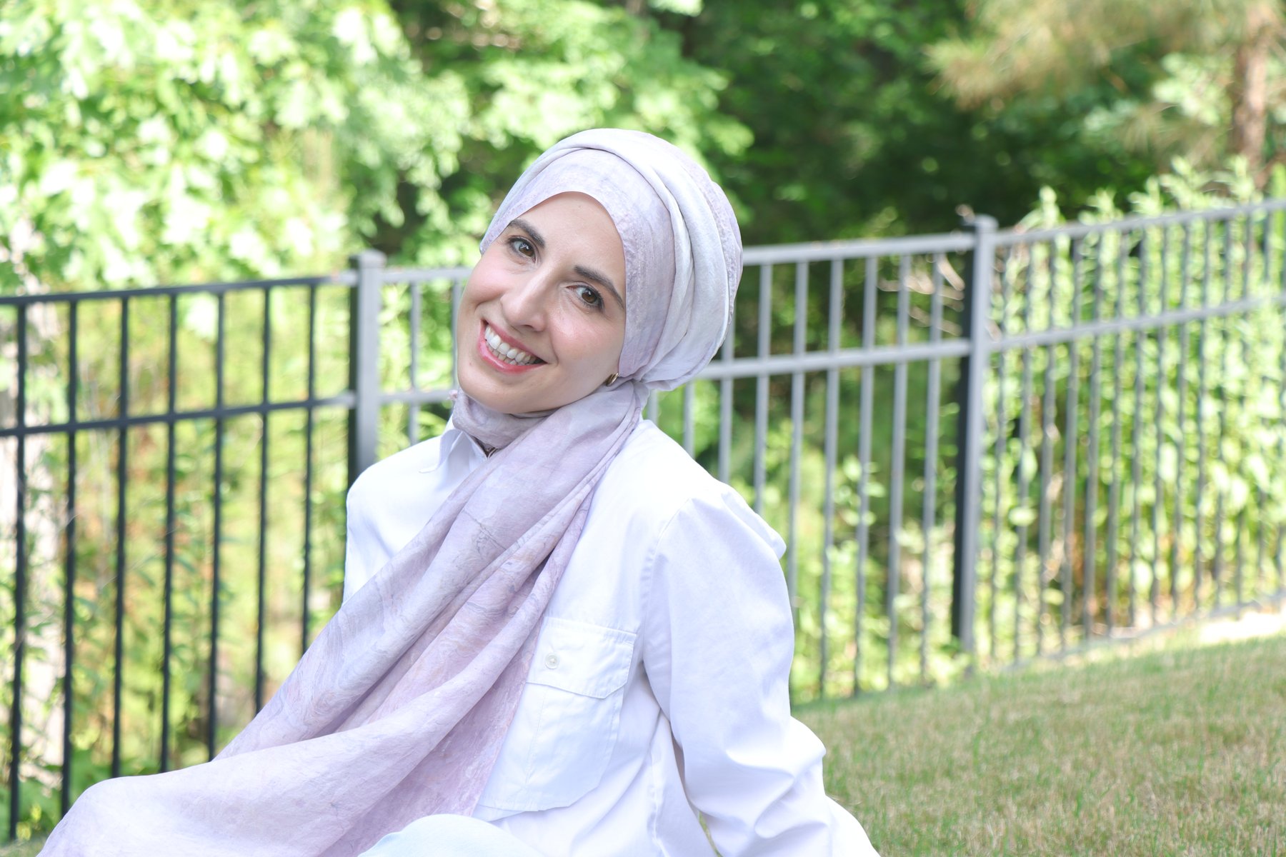 Portrait of Zeynep Guvenc seated in a garden, wearing one of her hand-marbled silk scarves