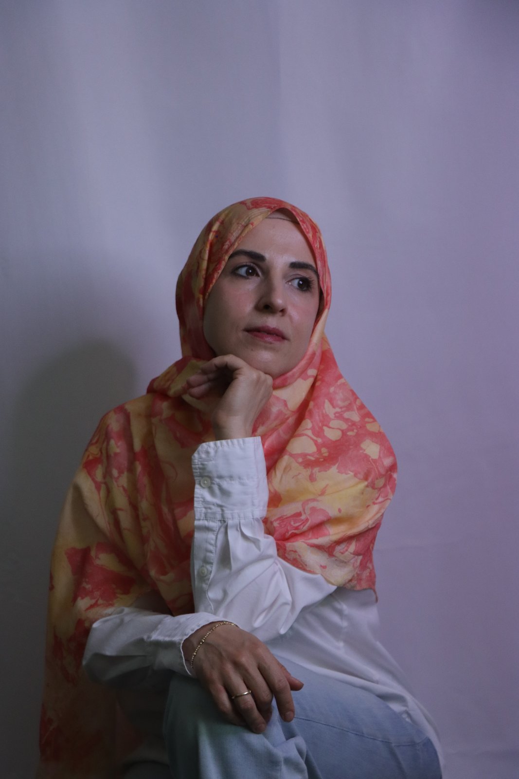 Hand-marbled silk scarf in coral, peach, and gold tones, worn draped