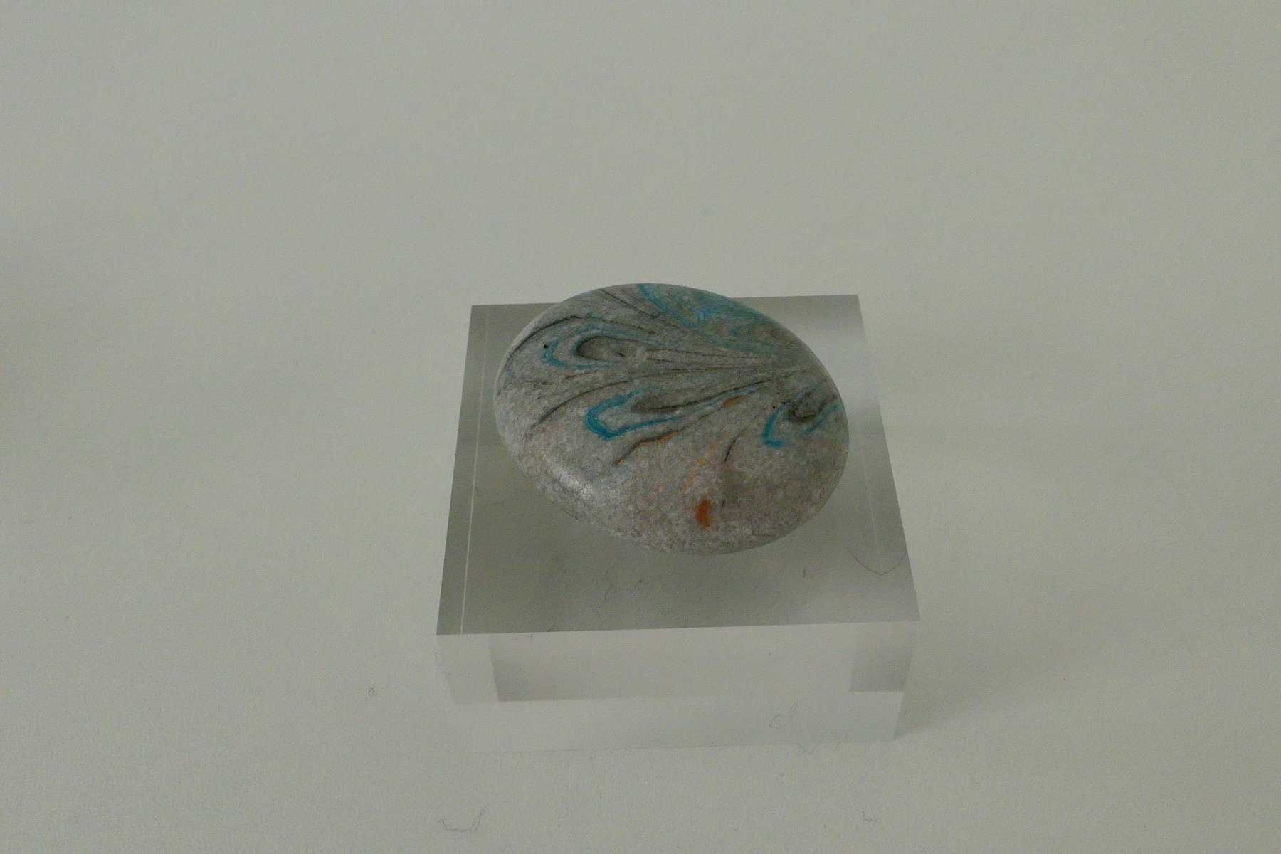 Small marbled stone with swirled pattern, displayed on a clear acrylic stand