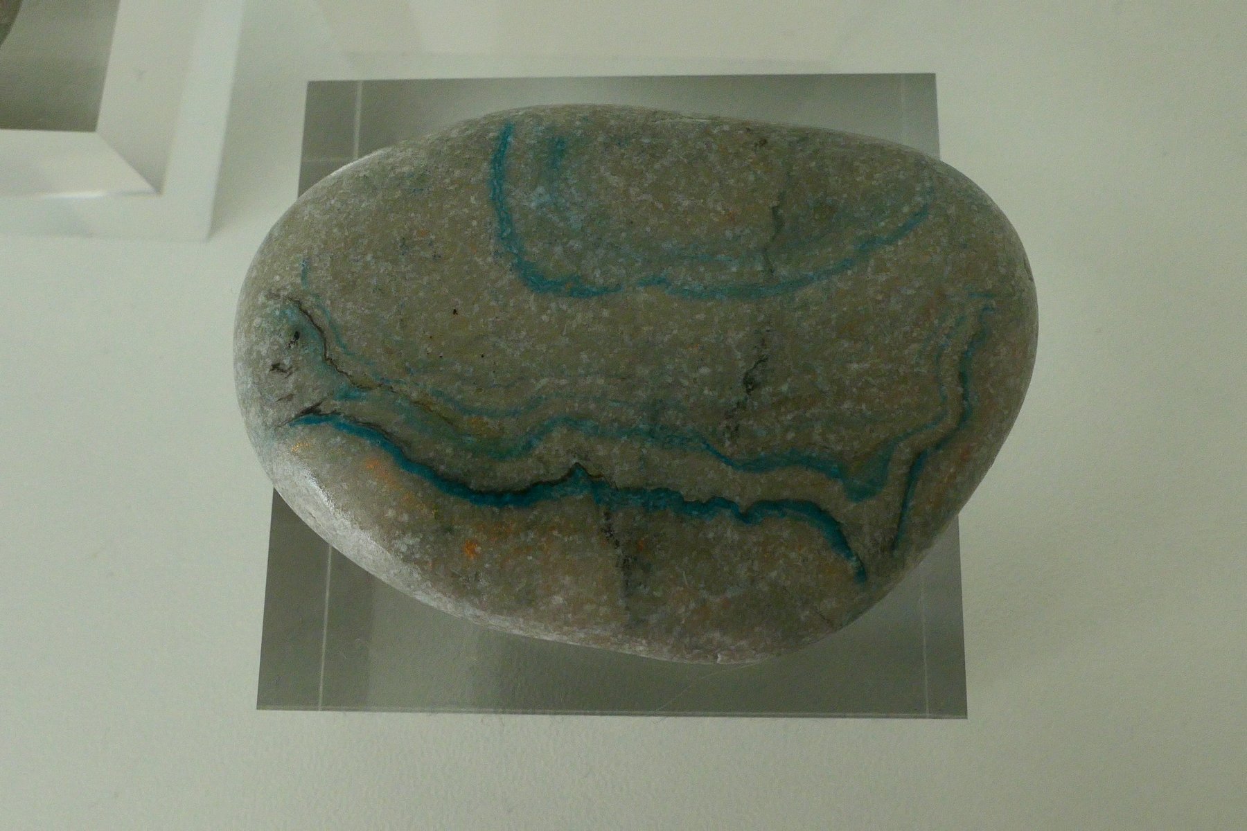 Large naturally weathered stone marbled with teal veining, on a clear acrylic stand