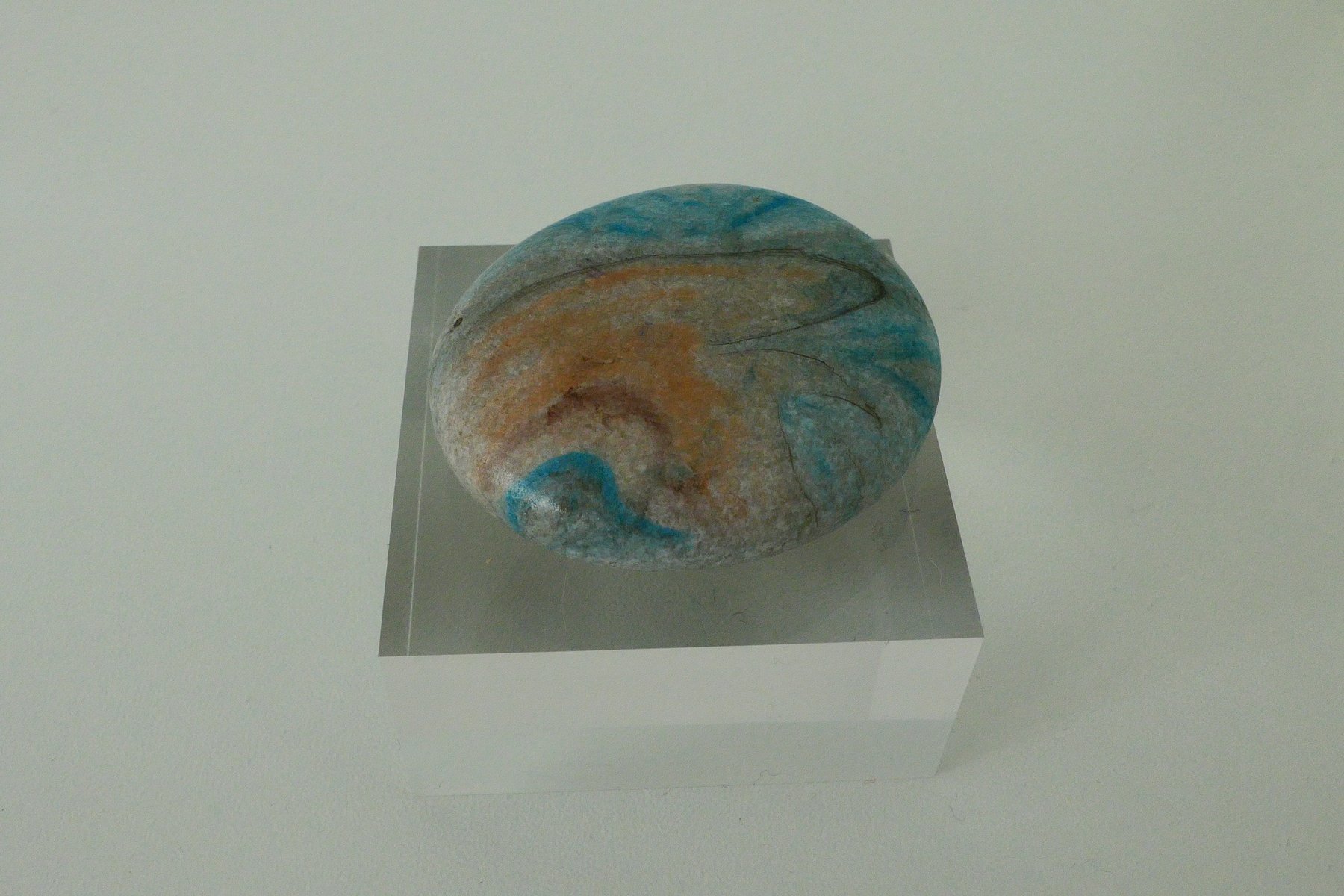Rounded naturally weathered stone marbled in blue and sand tones, on a clear acrylic stand