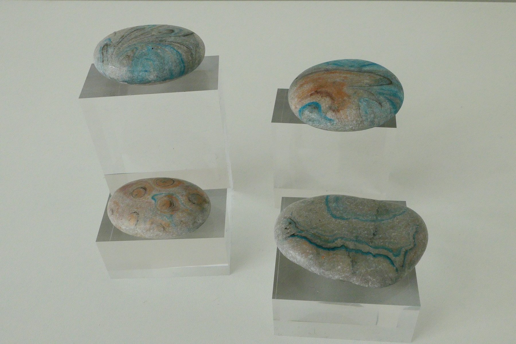 Group of marbled stones with teal and sand patterns, displayed on clear acrylic museum stands