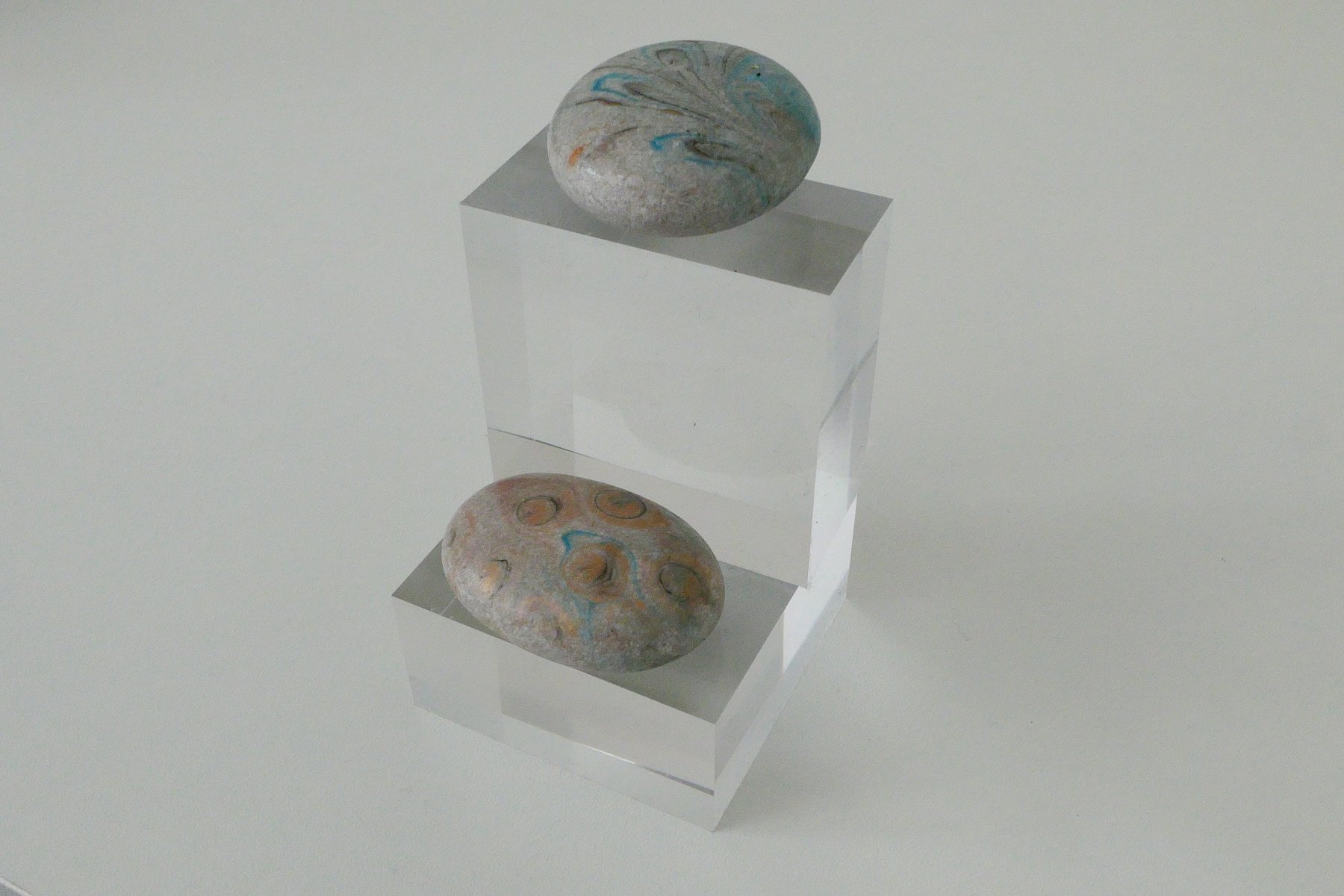 Two marbled stones displayed on stacked clear acrylic museum stands