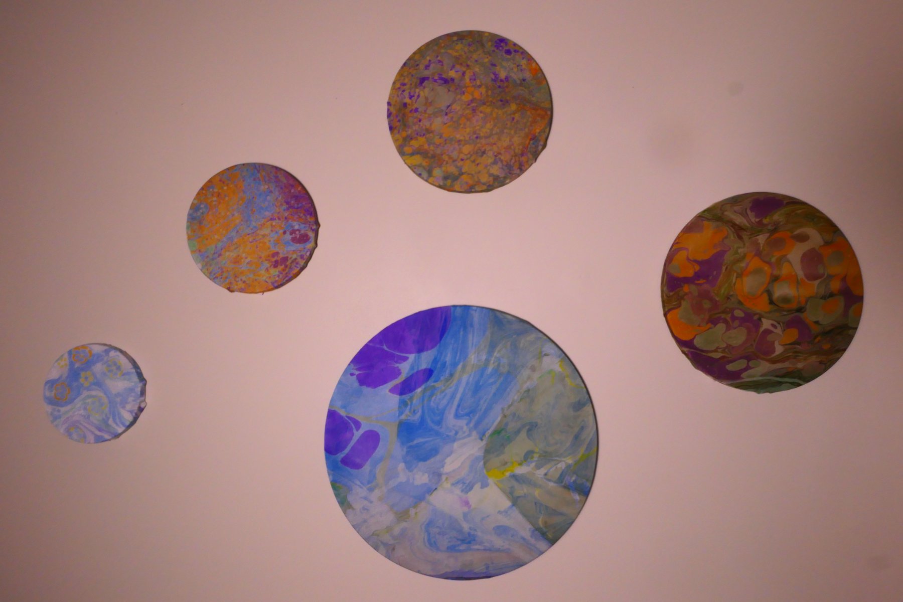 Wall installation of five marbled round panels of varying sizes and patterns