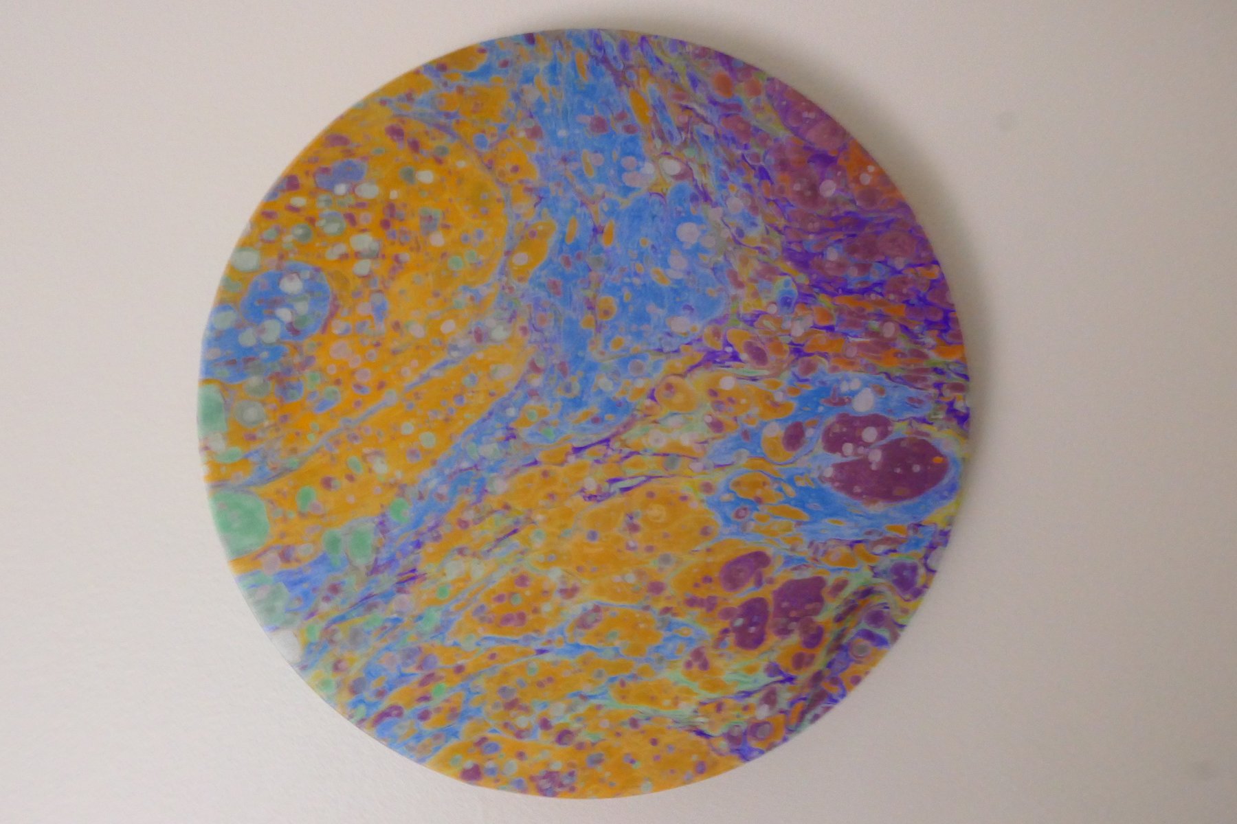 Round marbled wall panel with fine speckled pattern in orange, blue, and plum