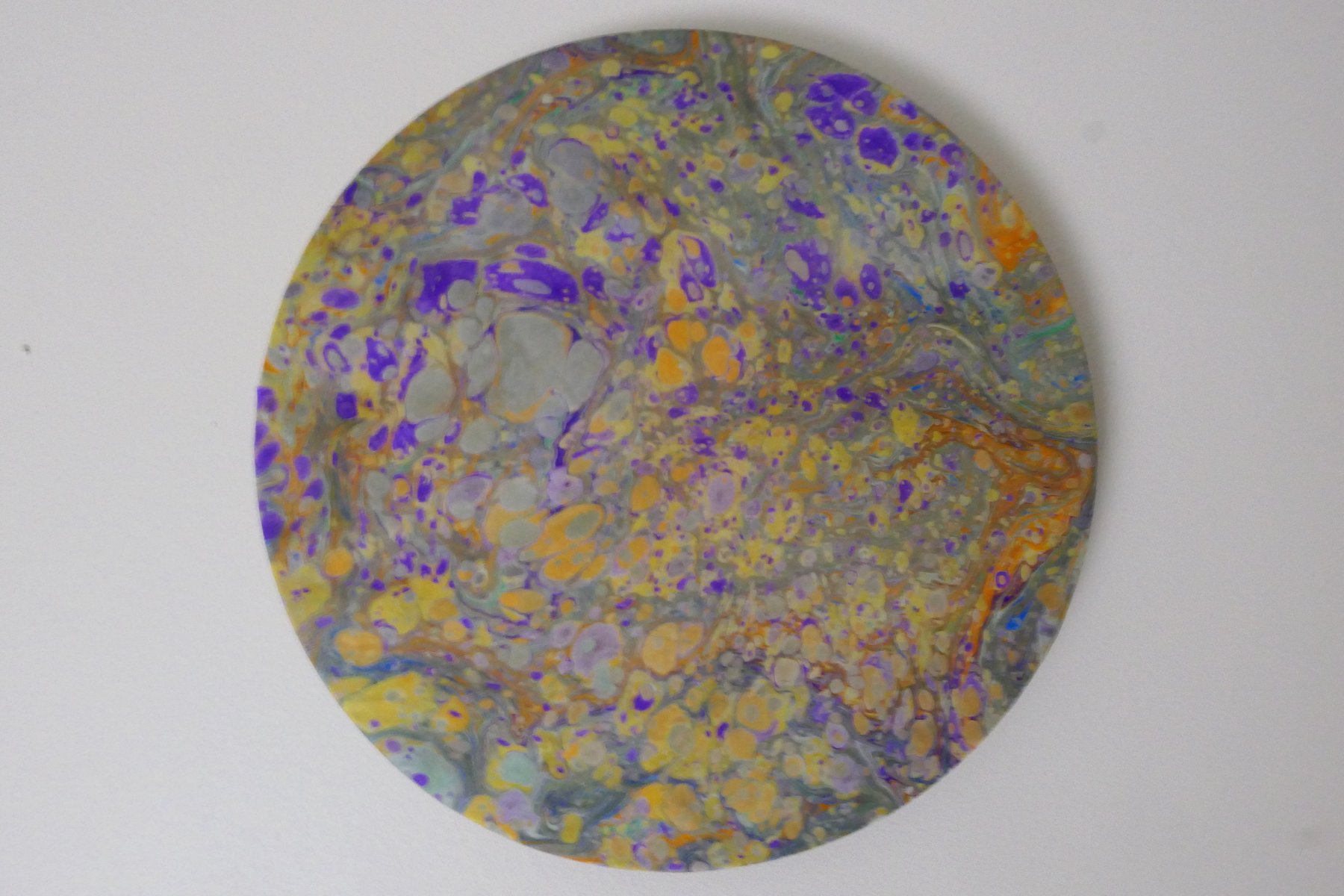 Round marbled wall panel with dense speckled pattern in violet, gold, and grey